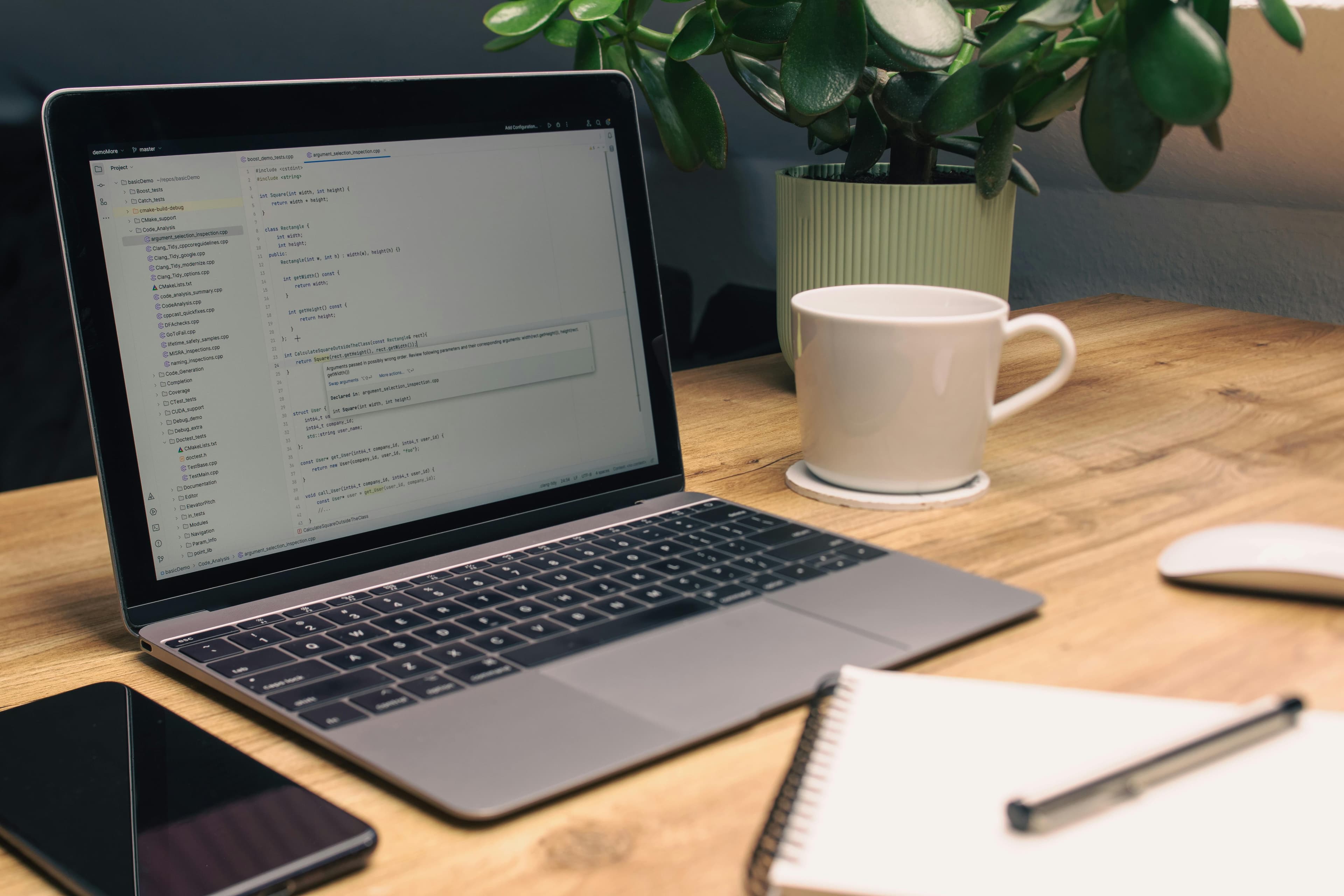 A laptop, coffee mug, and notebook on a timber desk.