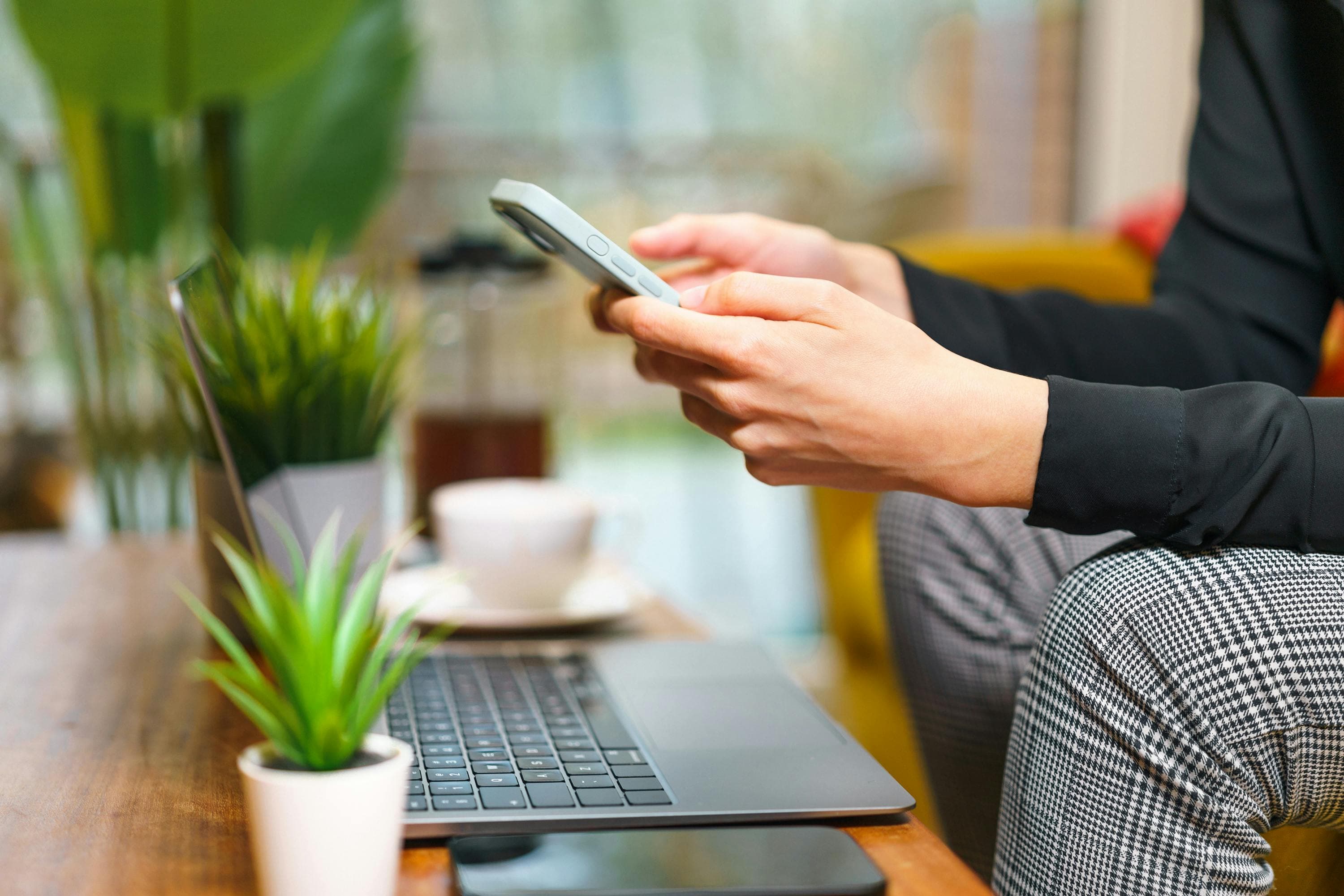 A business owner using a phone beside a laptop on a wooden table.